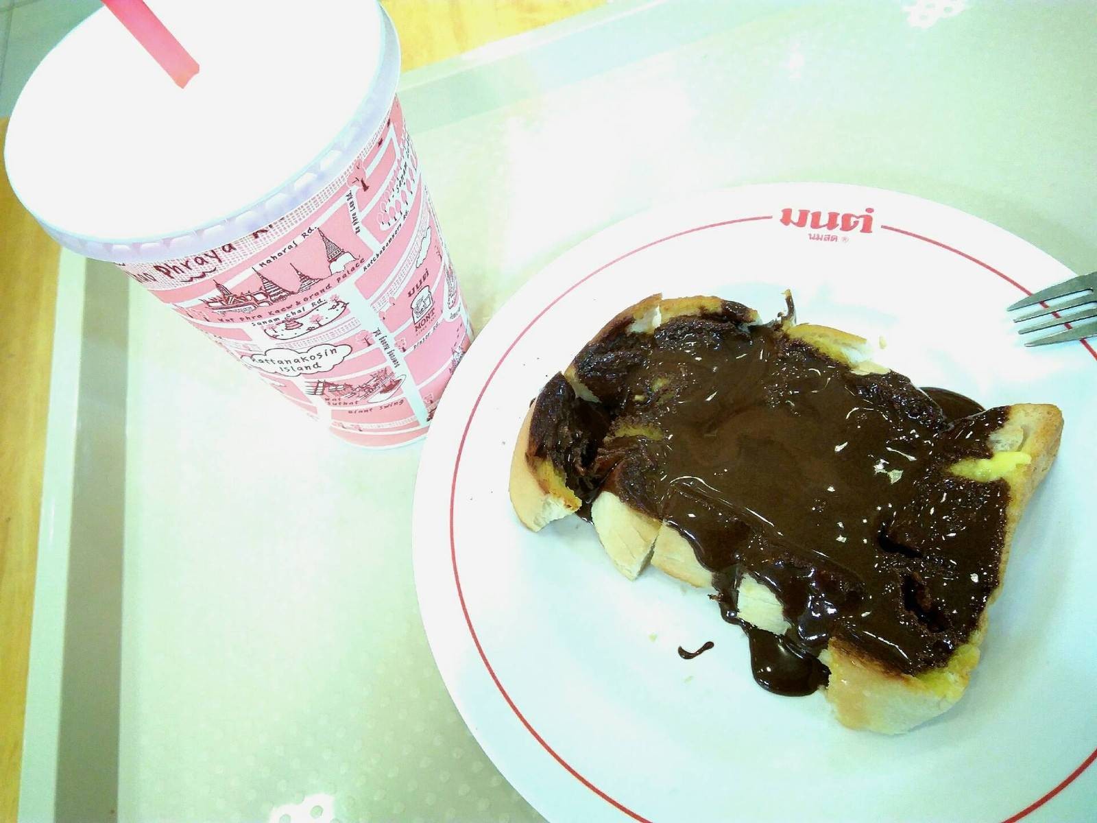 ขนมปังปิ้งราดช็อกโกแลตคู่กับนมสดเย็นแก้วลายชมพูของร้านมนต์ นมสด