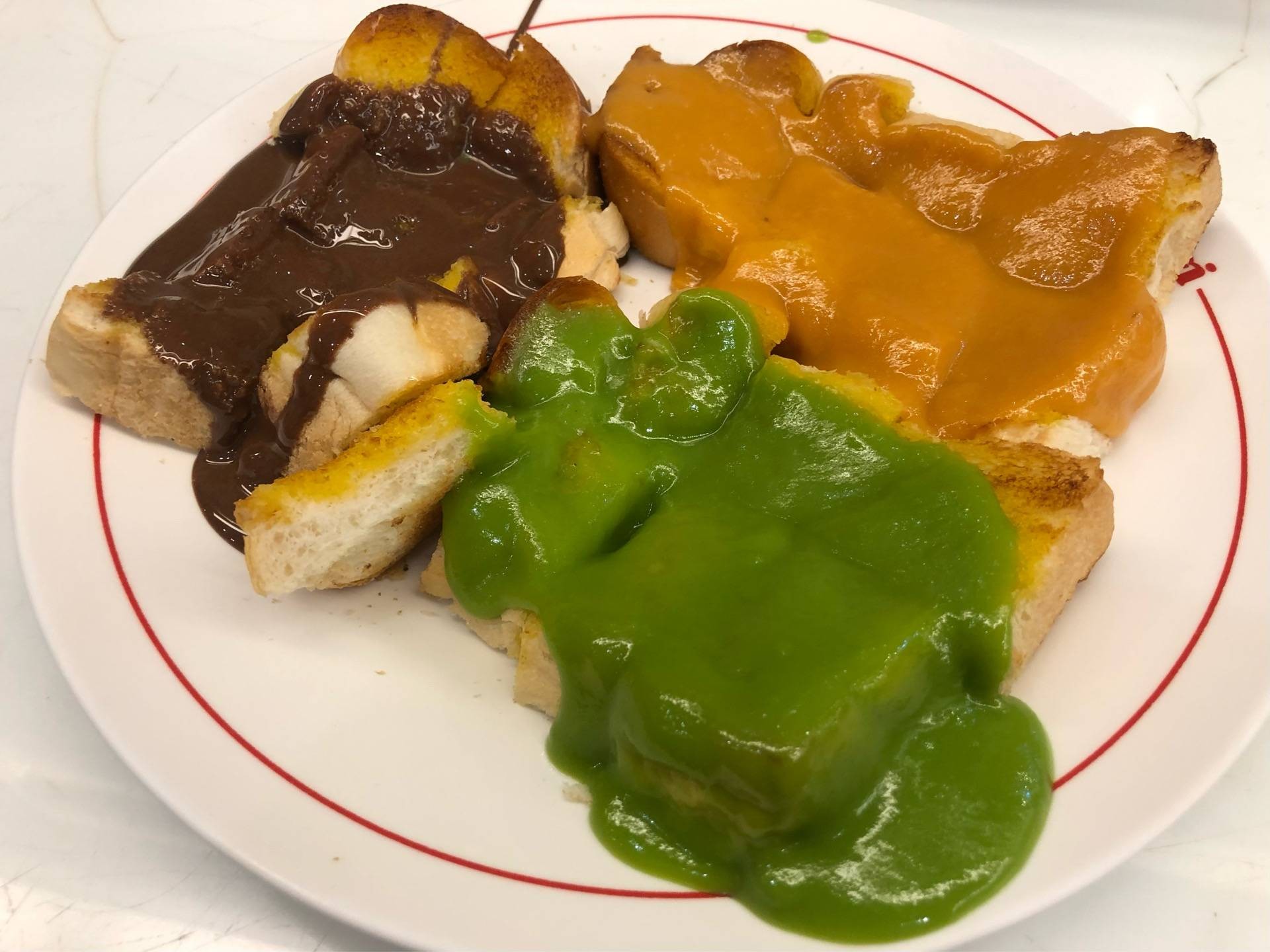 ขนมปังปิ้งราดสังขยา ช็อกโกแลต และใบเตย บนจานลายโลโก้ร้านมนต์ นมสด สาขาดินสอ
