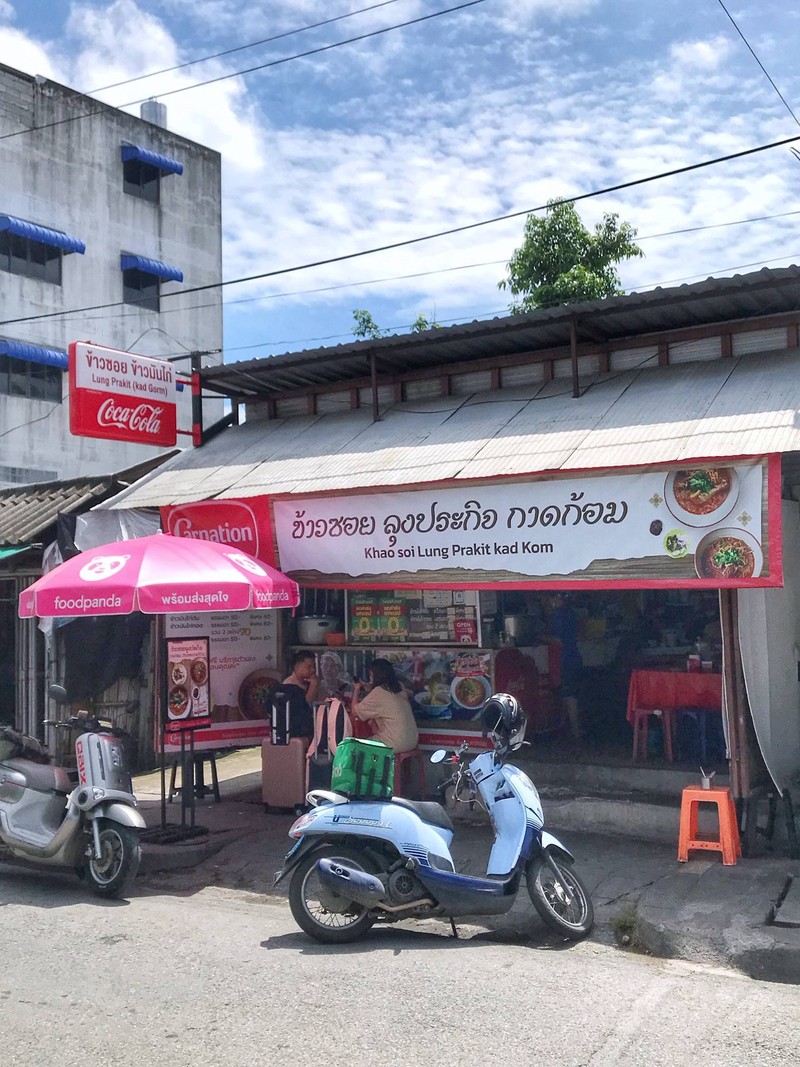 หน้าร้านข้าวซอยลุงประกิจ กาดก้อม ป้ายชื่อร้านและมอเตอร์ไซค์จอดหน้าร้าน