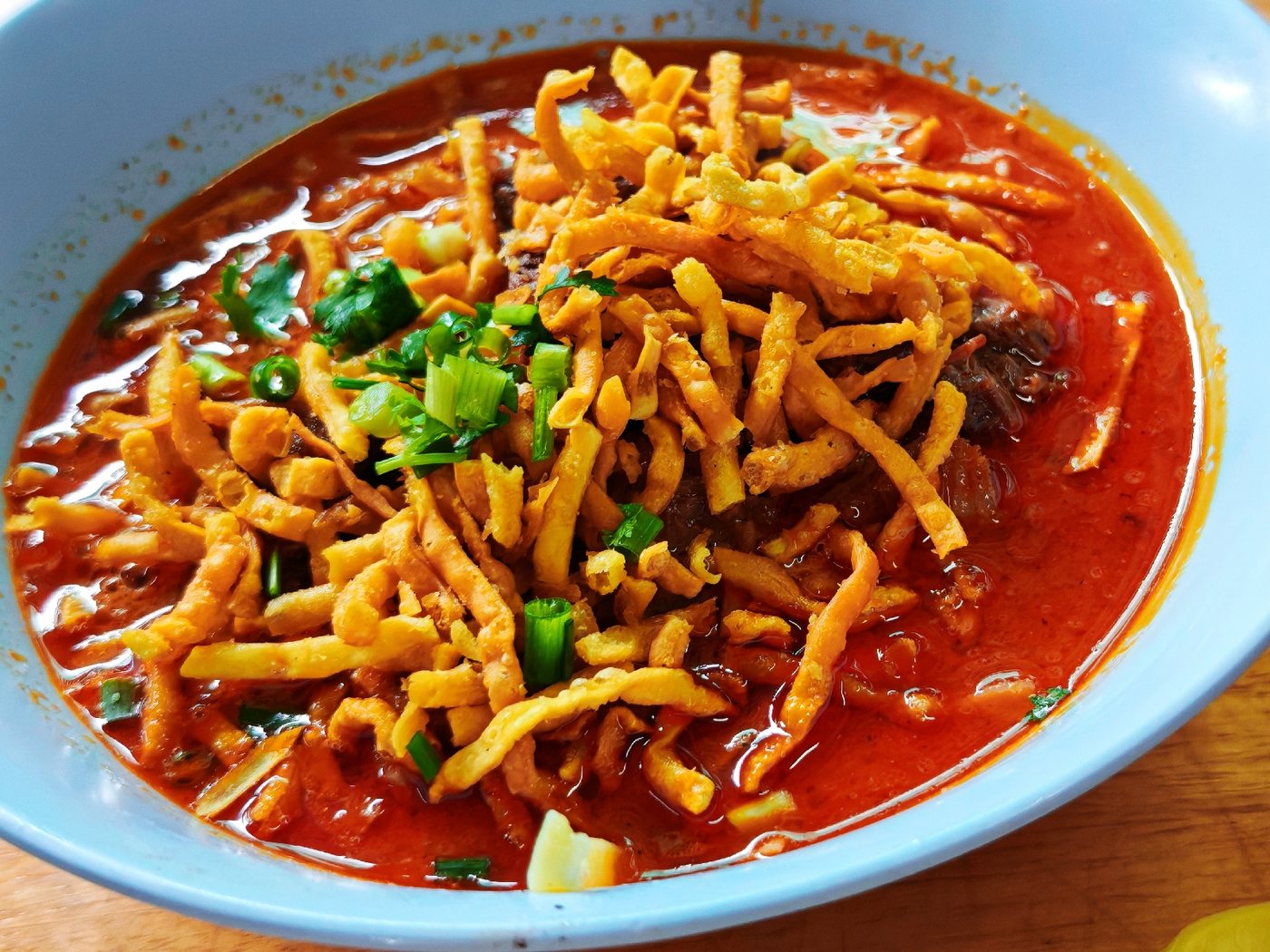 ชามข้าวซอยน้ำแกงเข้มข้นสีส้มแดง โรยเส้นบะหมี่ทอดกรอบ ของร้านข้าวซอยลุงประกิจ กาดก้อม เชียงใหม่