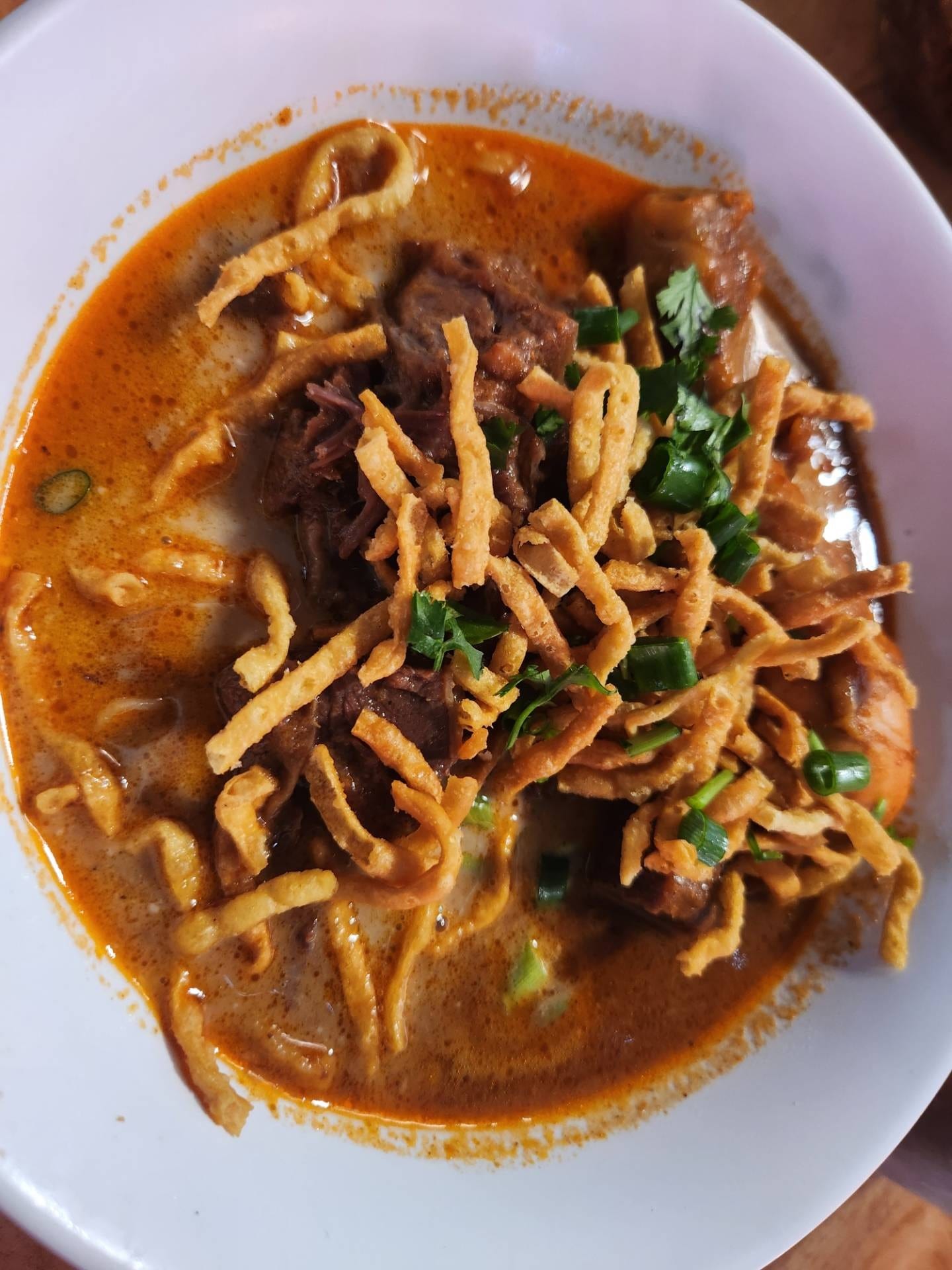 ข้าวซอยเนื้อ ร้านข้าวซอยลุงประกิจ กาดก้อม เชียงใหม่ น้ำแกงเข้มข้นสีส้มแดง โรยเส้นข้าวซอยทอดกรอบ
