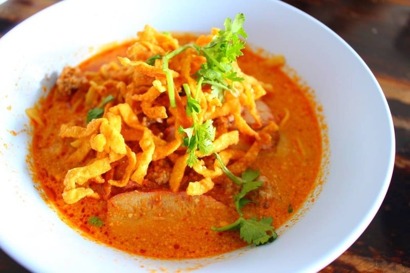 ข้าวซอยน้ำแกงสีส้มเข้มข้น โรยเส้นกรอบและผักชี