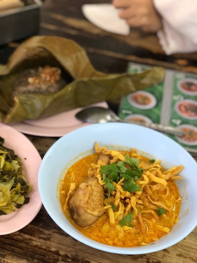 ข้าวซอยไก่บนโต๊ะในร้าน เสิร์ฟพร้อมข้าวเหนียวห่อใบตองและผักดอง