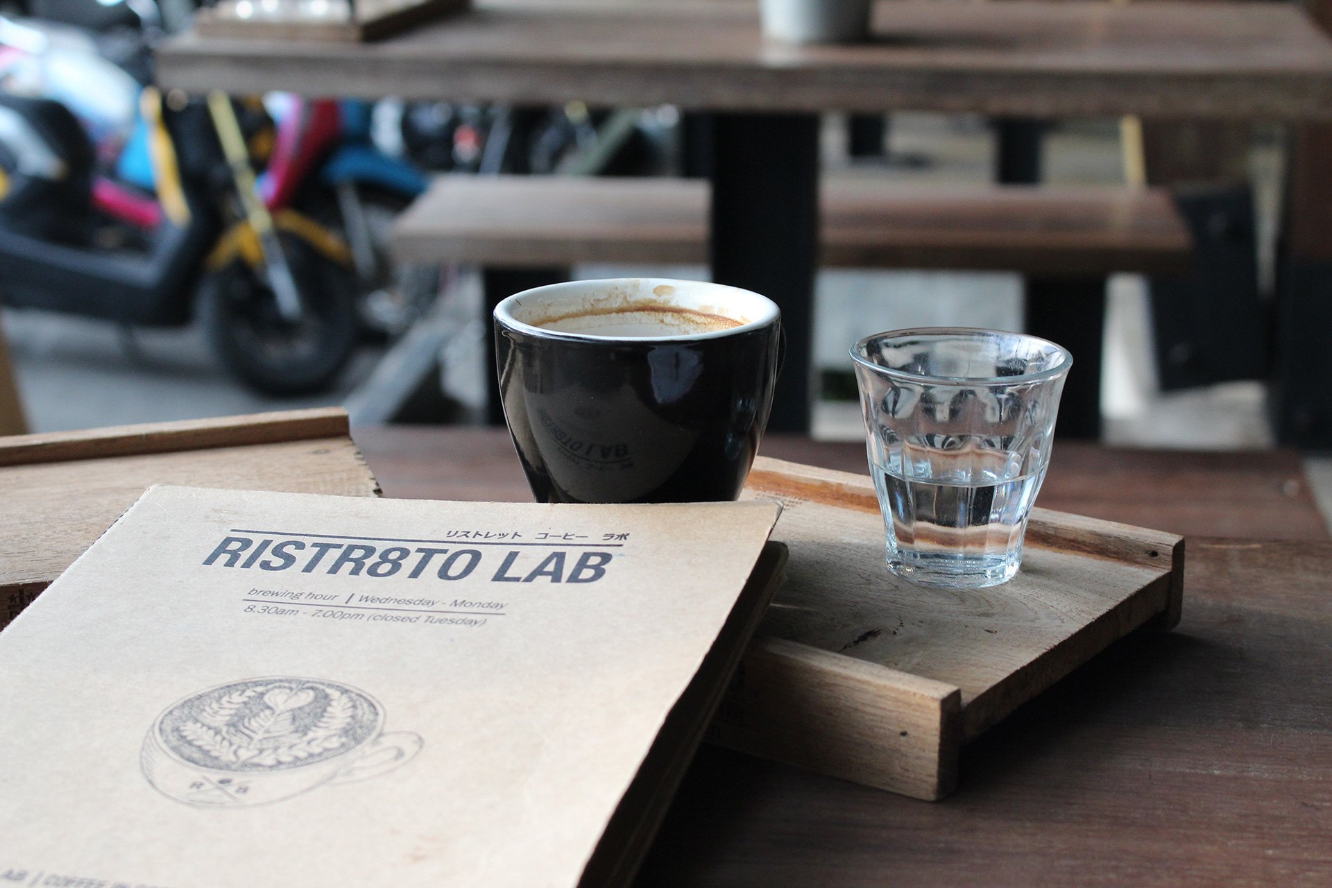 เมนูการ์ด RISTR8TO LAB วางคู่กับแก้วกาแฟและน้ำเปล่าบนถาดไม้ ร้าน Ristr8to เชียงใหม่