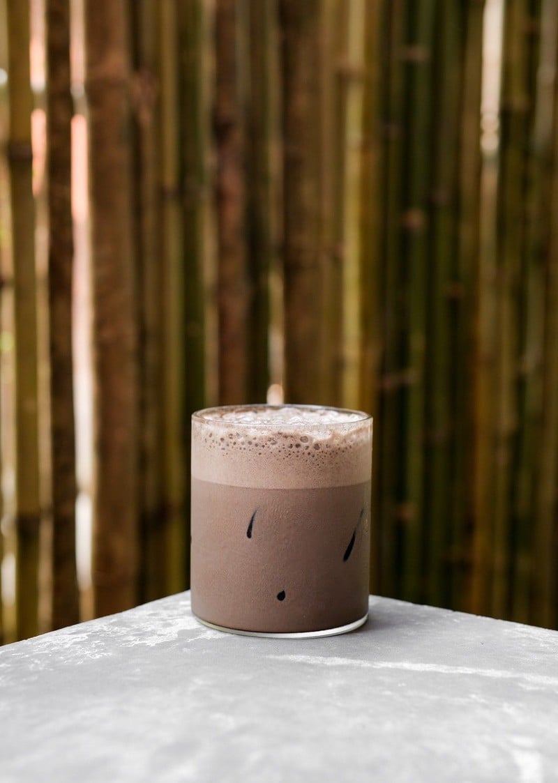 เครื่องดื่มแก้วเดียวตั้งบนโต๊ะปูนหน้ากำแพงไผ่ในคาเฟ่ The Baristro Asian Style