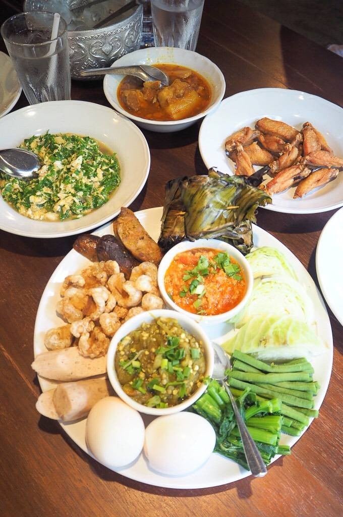 สำรับอาหารเหนือต๋องเต็มโต๊ะบนโต๊ะไม้สัก ไส้อั่ว แคปหมู น้ำพริกหนุ่ม น้ำพริกอ่อง ผักสด