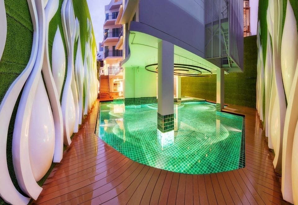 สระว่ายน้ำกึ่งกลางแจ้งของ Anajak Bangkok Hotel ผนังลายใบไม้อาร์ตเดโคและร่มเงา