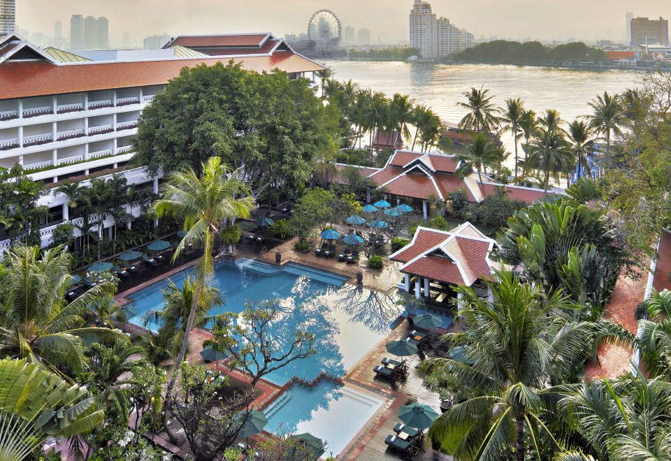 สระว่ายน้ำกลางแจ้งขนาดใหญ่ของ Anantara Riverside Bangkok ล้อมรอบด้วยสวนเขียวขจี