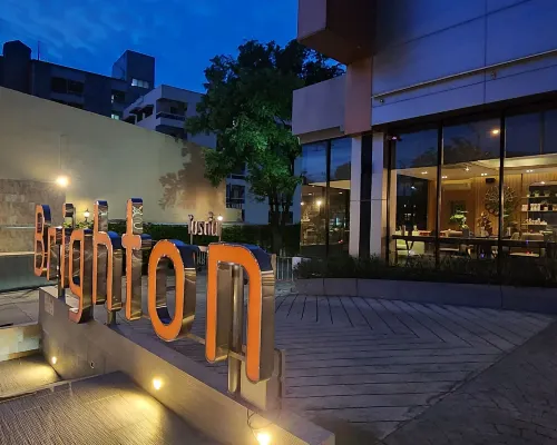Brighton Hotel Bangkok entrance at night — illuminated orange sign and bistro entrance