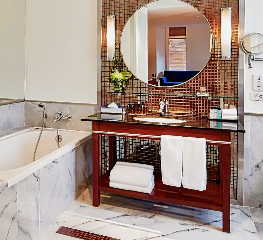 Triple Two Silom bathroom — marble bathtub, round mirror, copper mosaic tiles, plush towels