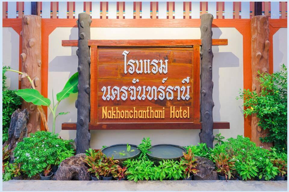 ป้ายไม้สลักชื่อโรงแรมนครจันทร์ธานี Nakhonchanthani Hotel ล้อมด้วยสวนต้นไม้เขียวเล็กๆ หน้าโรงแรม