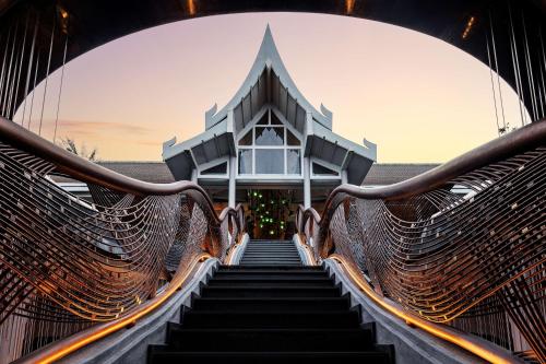 The curved woven-metal staircase of Banyan Tree Krabi climbing towards a Thai-roofed building at sunset