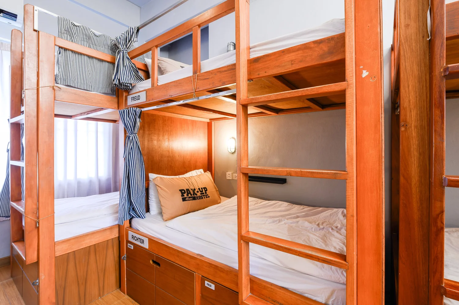 เตียงบังก์ไม้สักของ Pak-Up Hostel มีม่านปิดส่วนตัว ปลอกหมอนปัก Pak-Up