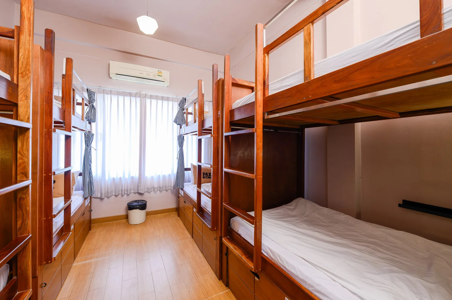 ดอร์มของ Pak-Up Hostel ห้องโปร่ง พื้นไม้ มีหน้าต่างและแอร์ เตียงบังก์ไม้สองชั้น