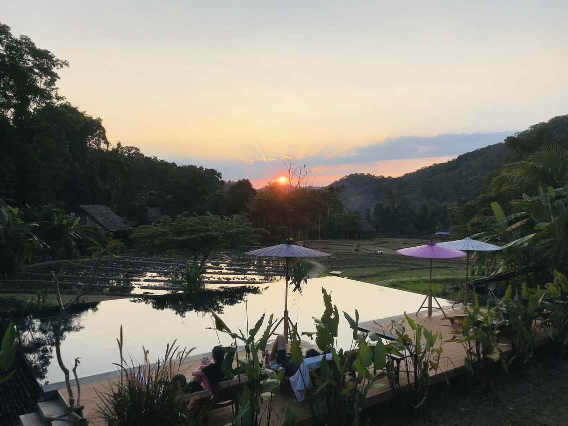 ระเบียงไม้ของกระท่อมพักมองออกไปเห็นทุ่งนาและสวนเขียวร่มรื่น