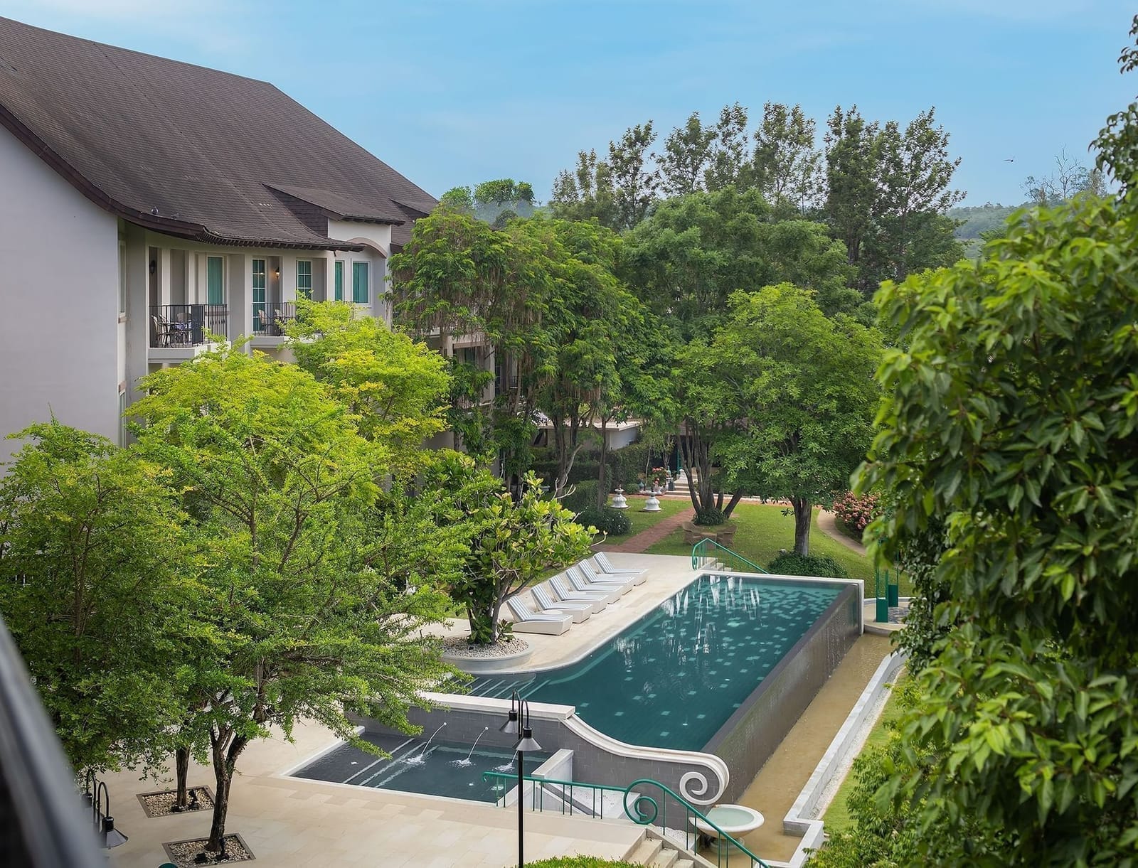 สระว่ายน้ำแบบ free-form ของ U Khao Yai ล้อมรอบด้วยอาคารสไตล์ฝรั่งเศสและสวนเขียว