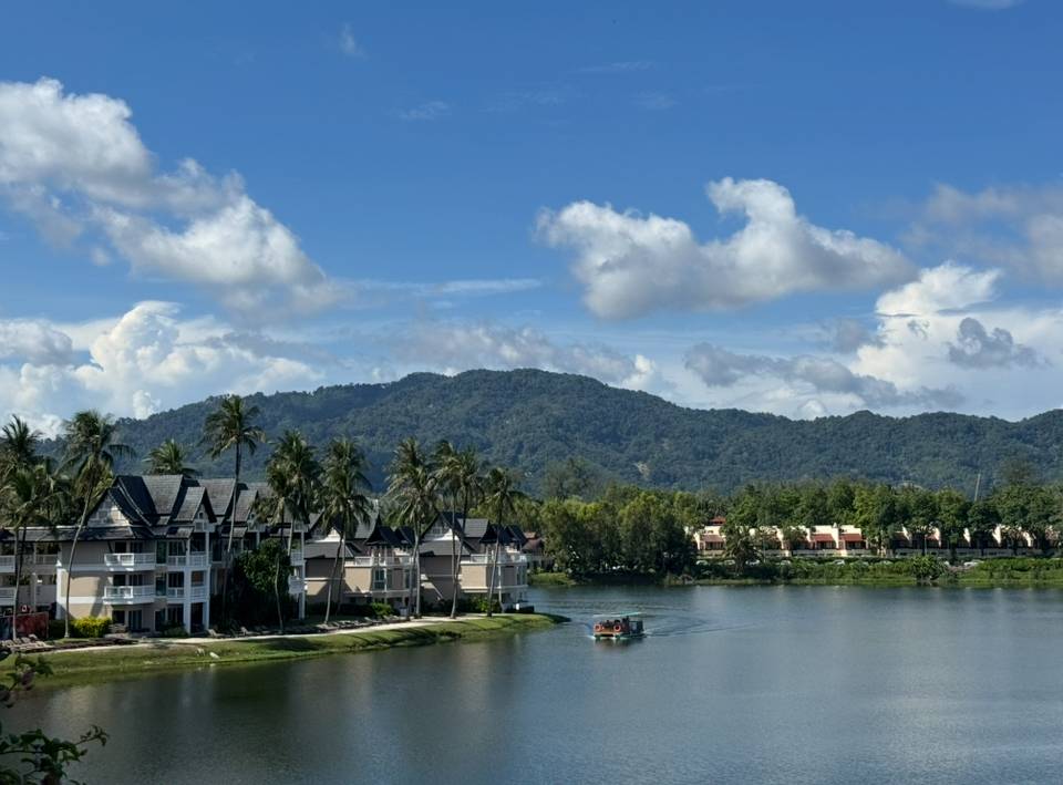 วิวลากูนกว้างของ Laguna Phuket พร้อมเรือรับส่งแล่นผ่านหน้าอาคาร Angsana และภูเขาเป็นฉากหลัง
