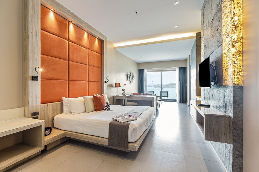 A Sea View Jacuzzi Junior Suite at Cape Sienna Phuket in wood and burnt-orange tones, with a balcony overlooking Kamala Bay