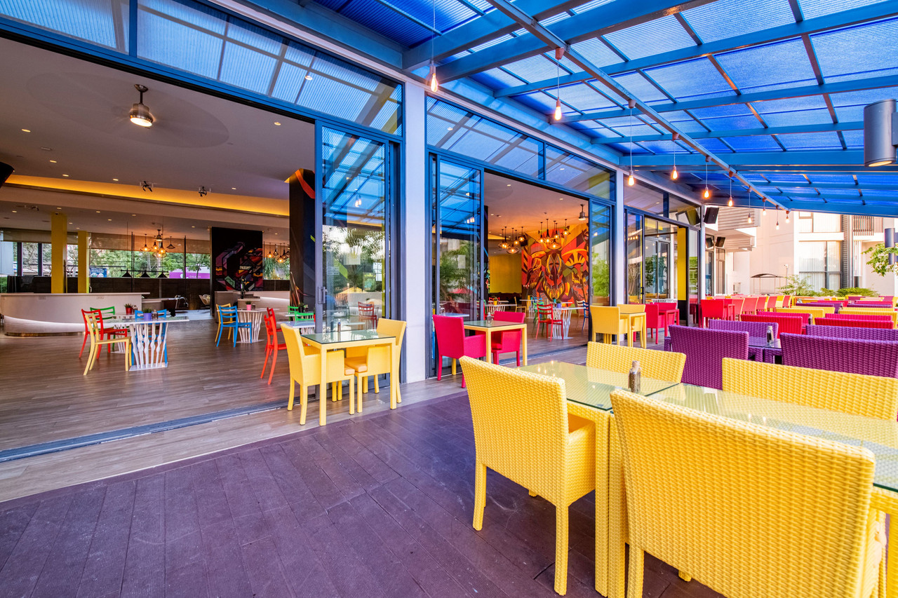 Vista Restaurant terrace at Cassia Phuket with yellow and purple wicker chairs under a blue canopy