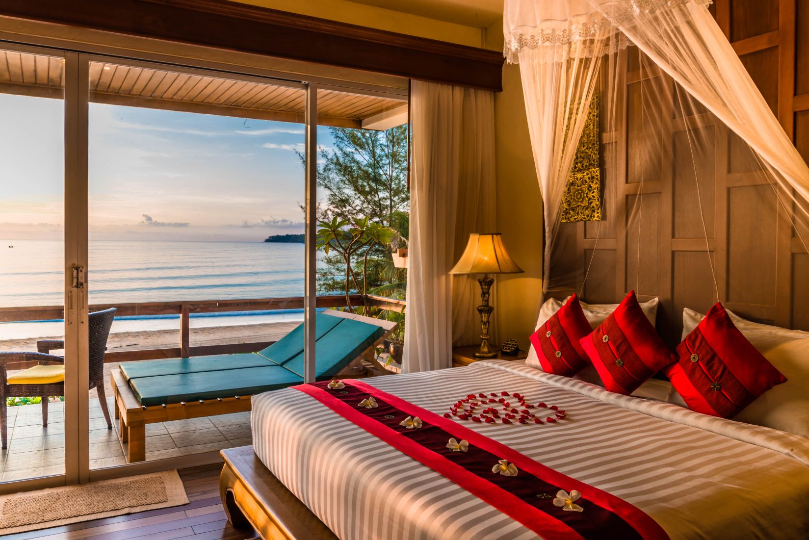 ห้องนอนสไตล์ไทยของ Layalina Hotel พร้อมเตียงสี่เสาและวิวทะเลกมลาจากหน้าต่างบานใหญ่