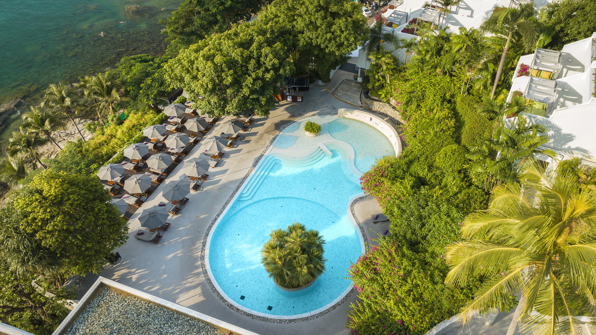 The Nai Harn's outdoor pool by the sea with shaded sun loungers overlooking Nai Harn Bay