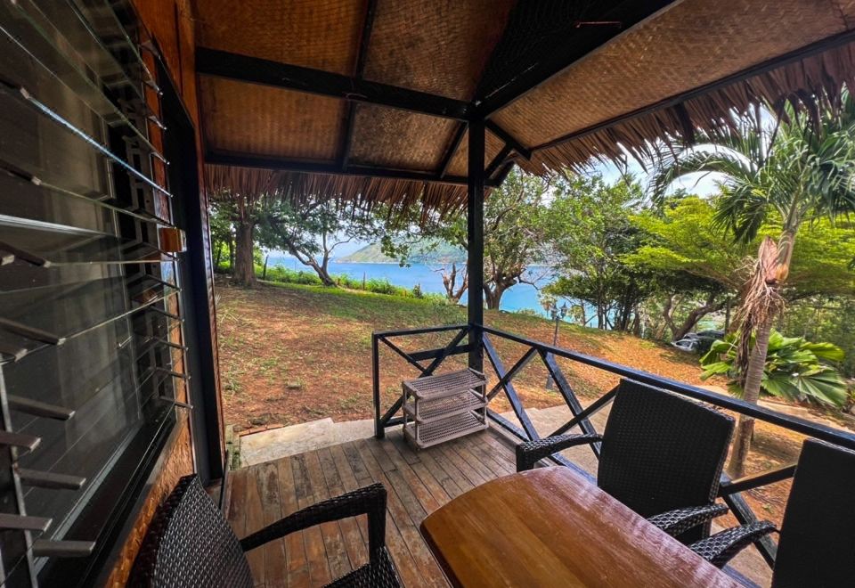 ระเบียงไม้ของบังกะโล Naiya Beach Bungalow มีเก้าอี้หวายและโต๊ะไม้ มองออกไปเห็นอ่าวทะเลสีครามและต้นไม้เขียว