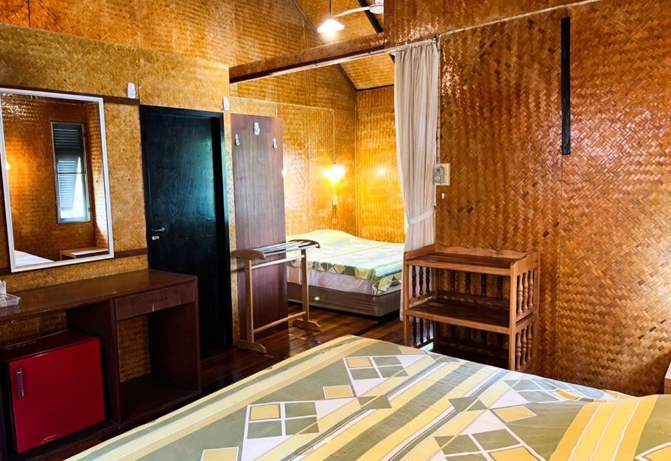 ภายในเรือนไม้ไผ่สานของ Naiya Beach Bungalow เตียงนอนกั้นด้วยม่าน โต๊ะเครื่องแป้งไม้และตู้เย็นเล็กสีแดง