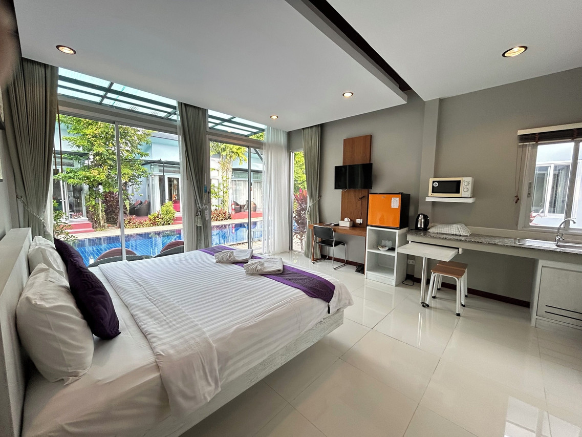 A Phu NaNa room with a king bed plus a microwave, fridge and desk nook, looking onto the pool through glass