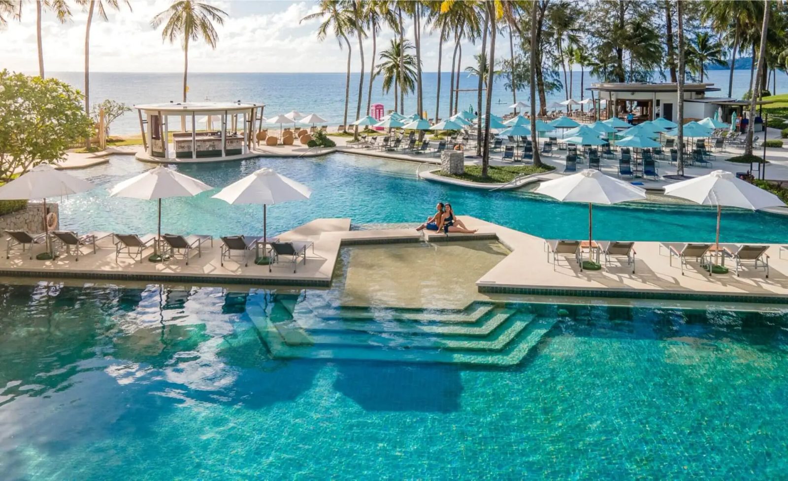 สระว่ายน้ำหลักของ SAii Laguna Phuket พร้อมสวิมอัพบาร์และร่มริมสระ มองเห็นหาดบางเทาด้านหลัง