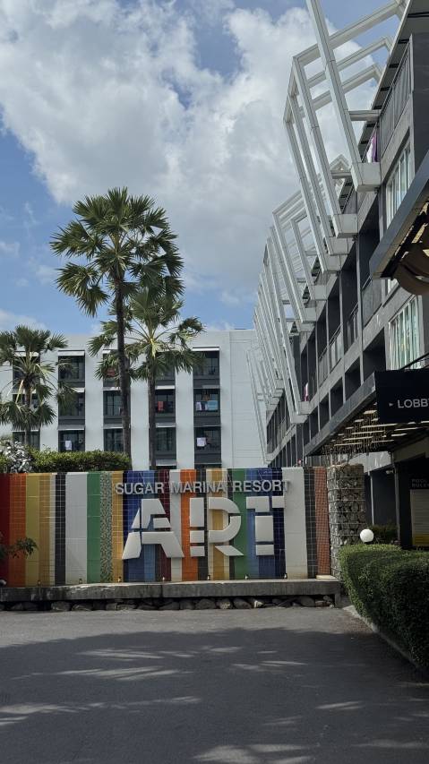 The colourful mosaic wall reading SUGAR MARINA RESORT ART at the hotel entrance, with tall fan palms