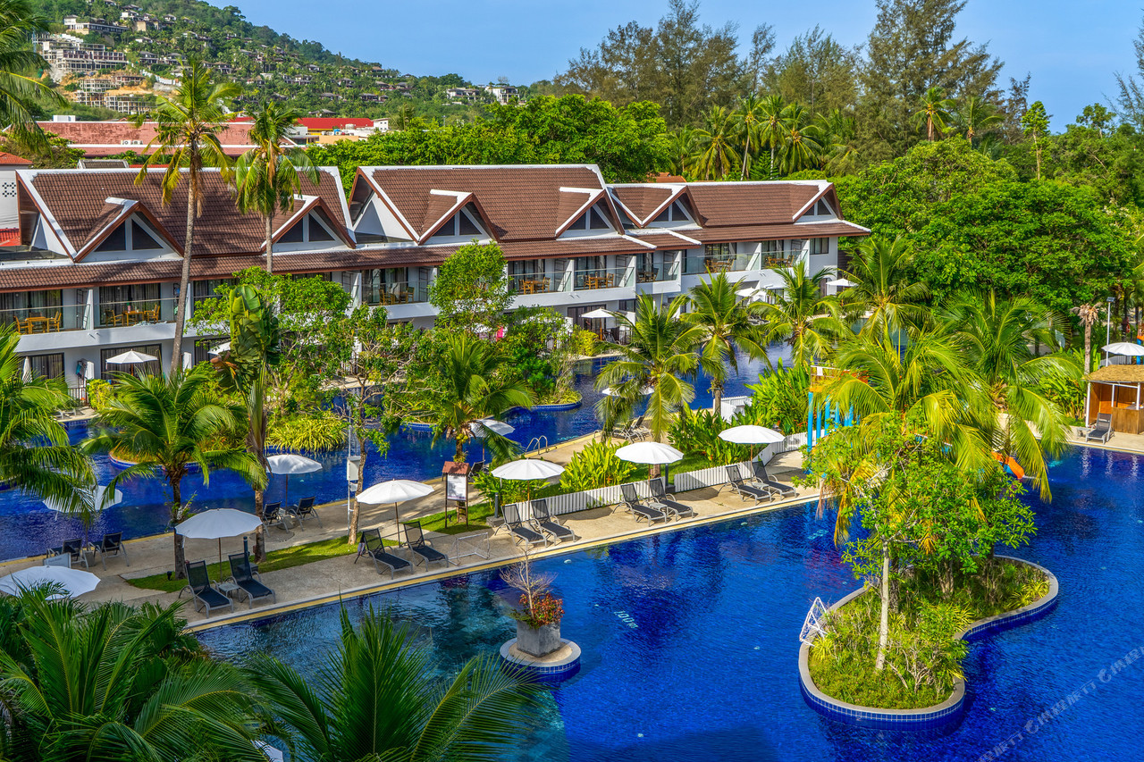 อาคารห้องพักหลังคาทรงไทยเรียงตามแนวสระลากูนของ Sunwing Kamala Beach โดยมีเนินเขากมลาเป็นฉากหลัง