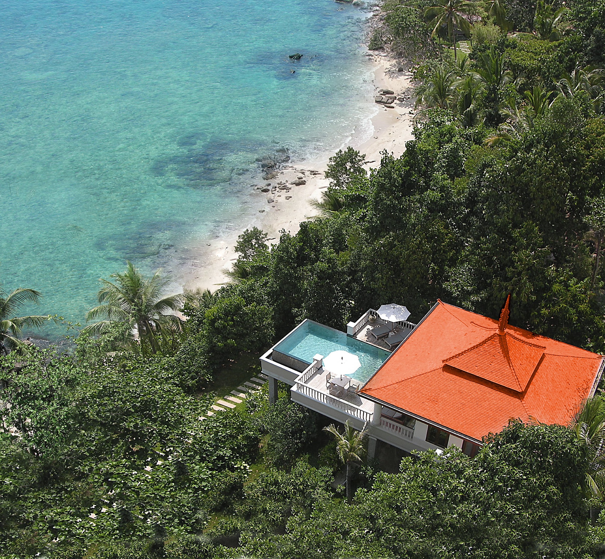 มุมสูงของ Ocean Front Pool Villa หลังคาสีส้มอิฐของ Trisara เหนือหาดส่วนตัวและน้ำทะเลใสของอ่าว