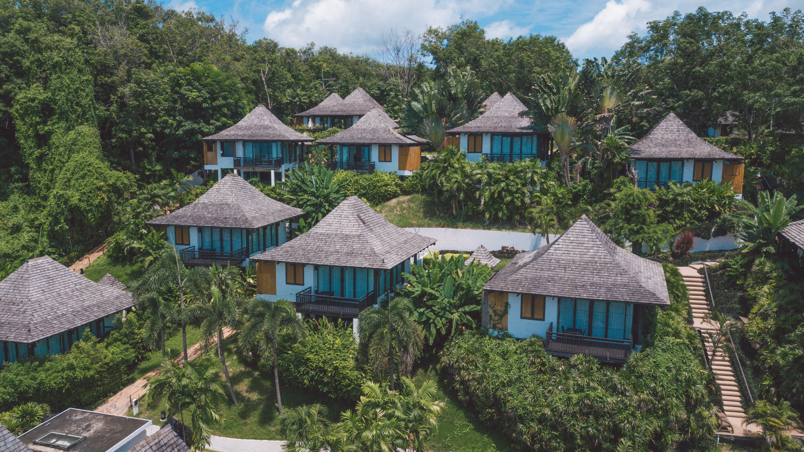 Standalone timber-roofed villas at The Vijitt arranged across a green garden slope above Friendship Beach in Rawai