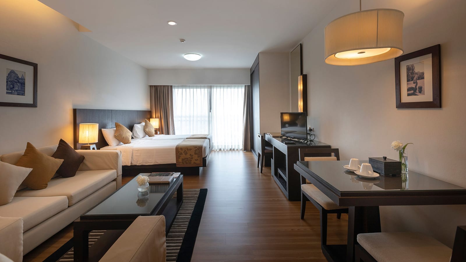 ห้อง Studio Suite ของ Kantary Hotel Kabinburi ปราจีนบุรี โทนไม้เข้มอบอุ่น มีโซฟา มุมรับประทานอาหาร โต๊ะทำงาน และระเบียงรับแสง