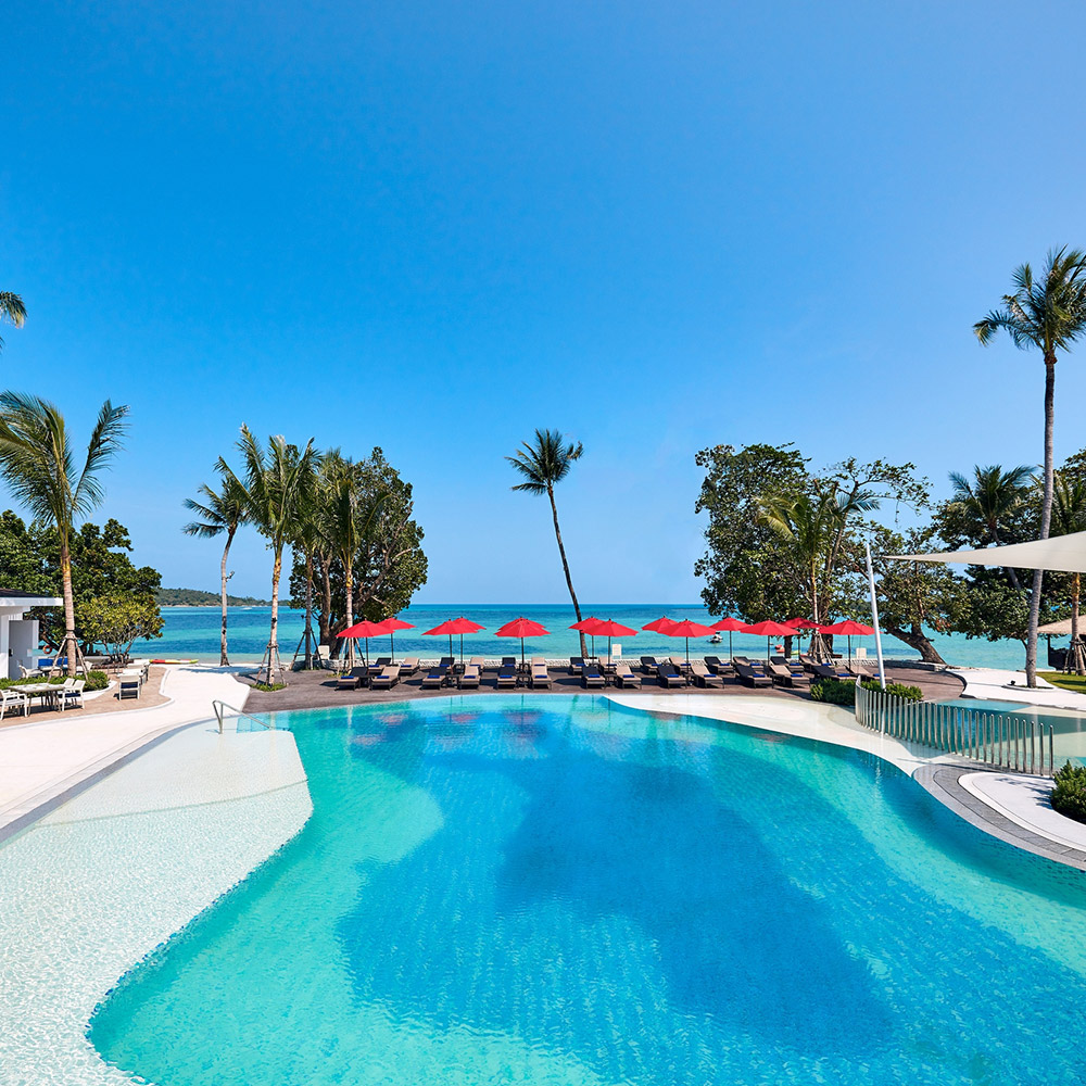 สระว่ายน้ำแบบฟรีฟอร์มของ Amari Koh Samui ล้อมด้วยสวนเขตร้อนและเก้าอี้อาบแดด