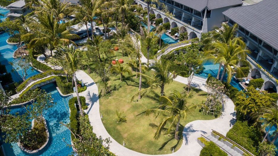 สระว่ายน้ำทรงคดเคี้ยวคล้ายแม่น้ำวนผ่านสวนเขตร้อนของ Meliá Koh Samui ขนาบด้วยอาคารห้องพัก