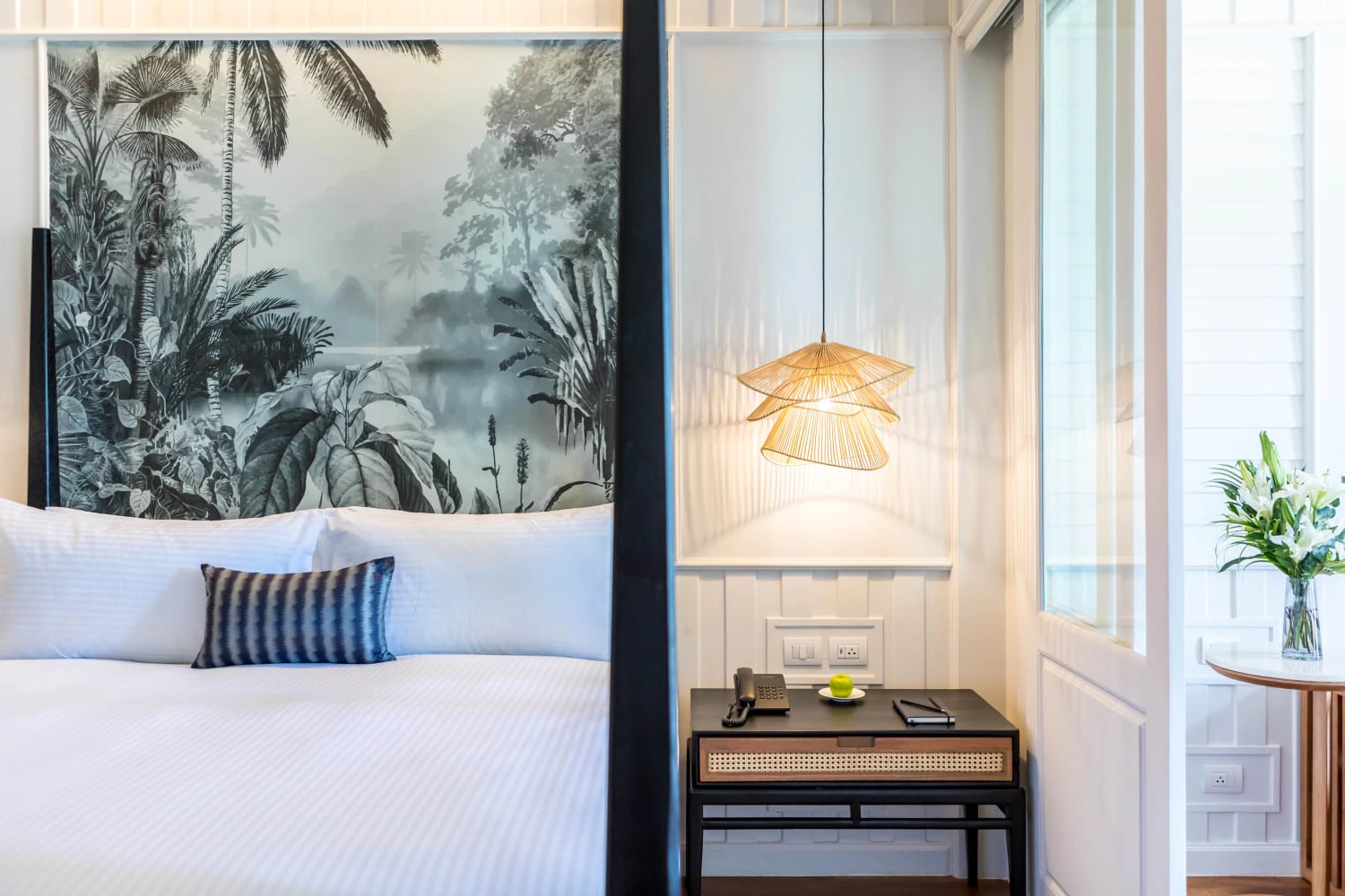 A colonial-style guestroom at Outrigger Koh Samui with a tropical-forest headboard mural and a woven rattan pendant lamp
