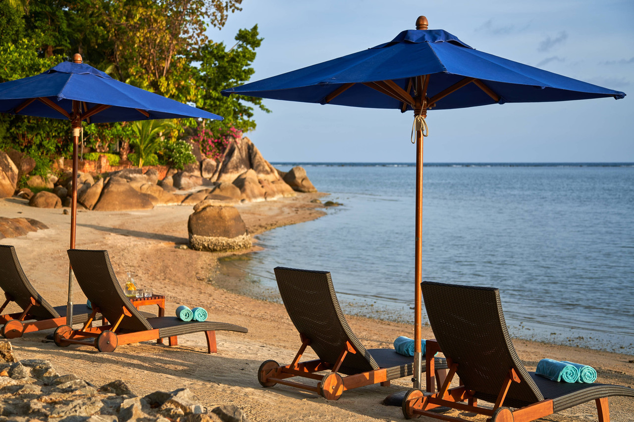 Beachfront loungers under blue umbrellas at Renaissance Koh Samui by the sea at the north end of Lamai Beach