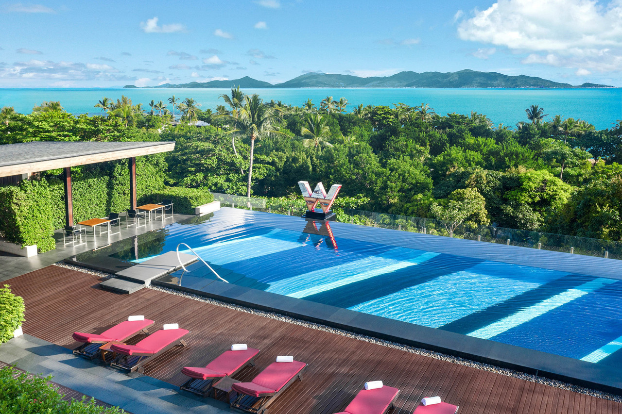 อินฟินิตี้พูลของบาร์ WOOBAR ที่ W Koh Samui ยื่นออกไปเหนือทะเล มีตัวอักษร W กลางสระและเก้าอี้อาบแดดสีชมพู