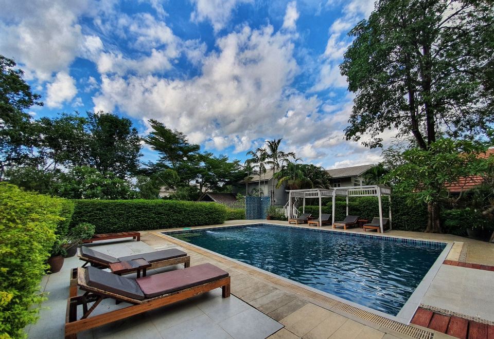 สระว่ายน้ำกลางแจ้งในสวนของ Tharaburi Resort ล้อมรอบด้วยต้นไม้เขียว
